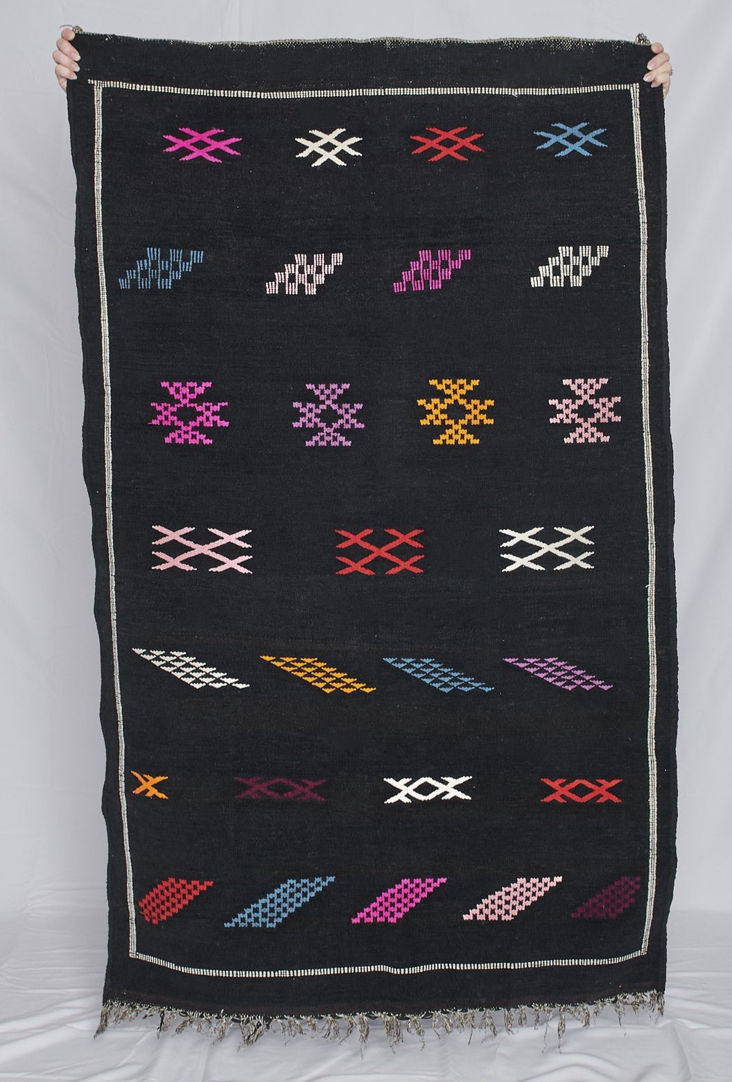 Moroccan Kilim rugs are handmade by women artisans in Morocco to be a very soft wool blend and a thin, flatweave style. Colorful, bright and vibrant colors for your living room, under dining table, or anywhere else for unique, ethnic home decor. Authentic Morocan, Morrocan style rug, black with bright geometric pattern.